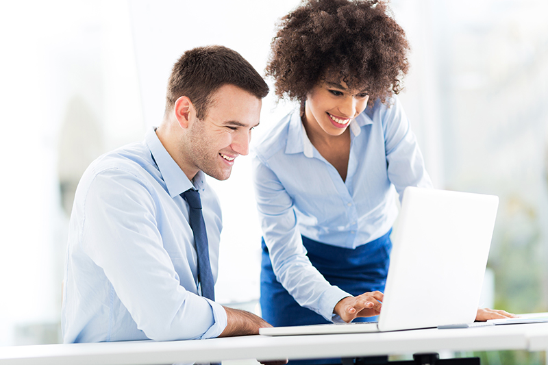 Een man en een vrouw in zakelijke kleding kijken samen naar een laptop, terwijl ze lachen en informatie delen.